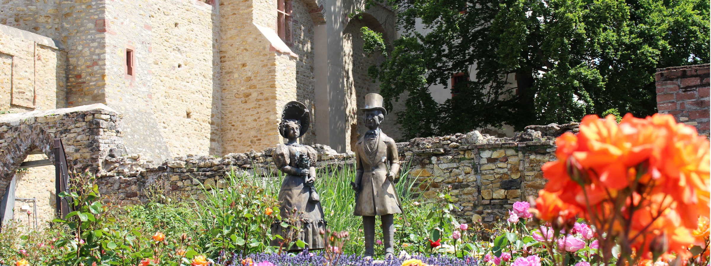 Das Biedermeierpärchen im Sonnenschein. Das bronzerne Biedermeierpaar im Sonnenscheint zwischen blühenden Rosen.