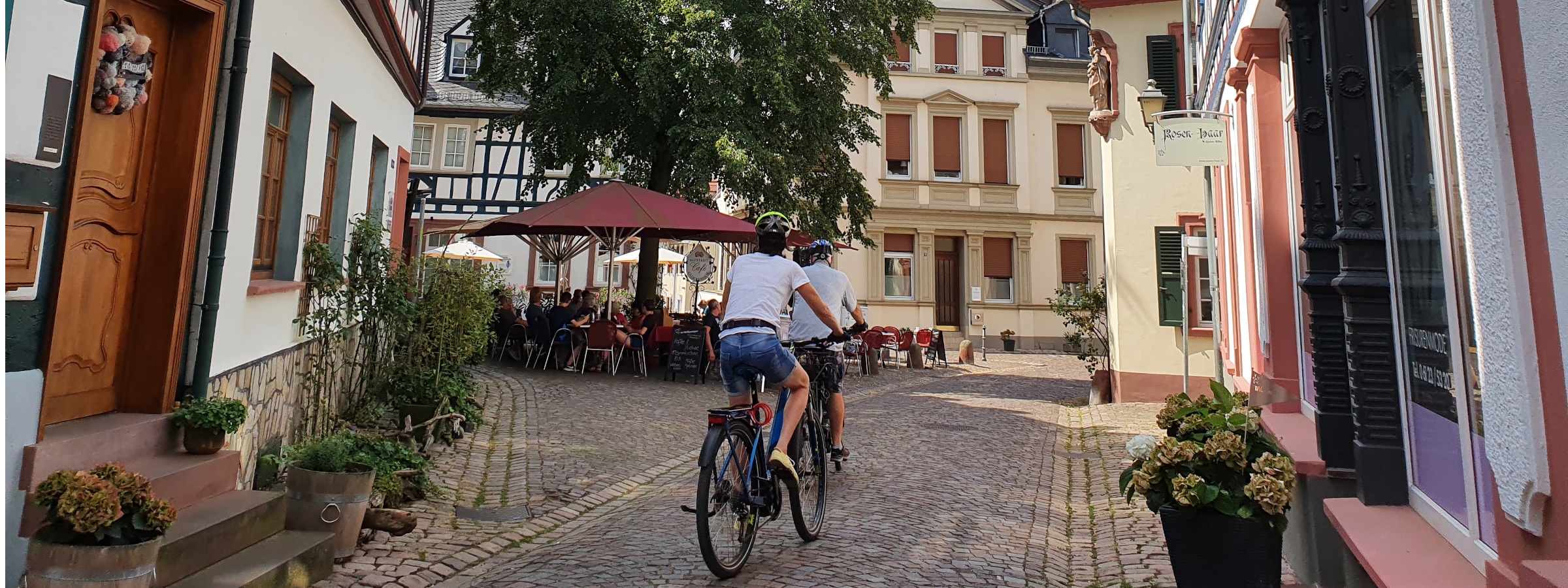 Eine Frau und ein Mann sind von hinten zu sehen, wie sie durch die Altstadt radeln.