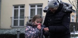 Kleines Mädchen riecht an einer Blume, neben ihr steht eine Frau und hält ihre Hand.