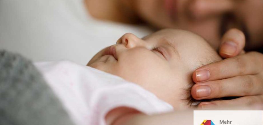 Symbolbild schlafendes Baby mit Frau im Hintergrund