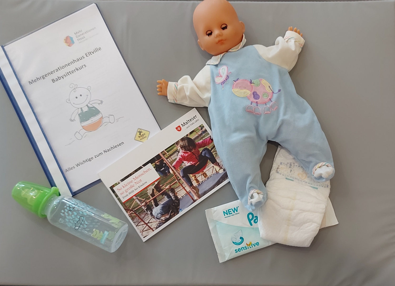 Utensilien des Babysitterkurses wie Puppe, Babyflasche und Infomappe