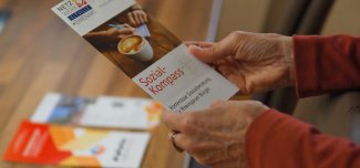 Hände halten einen Flyer vom Sozialkomass, im HIntergrund liegen weitere Angebotsflyer.