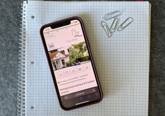 Ein Handy liegt auf einem weißen Block, geöffnet ist die Internetseite des MGHs