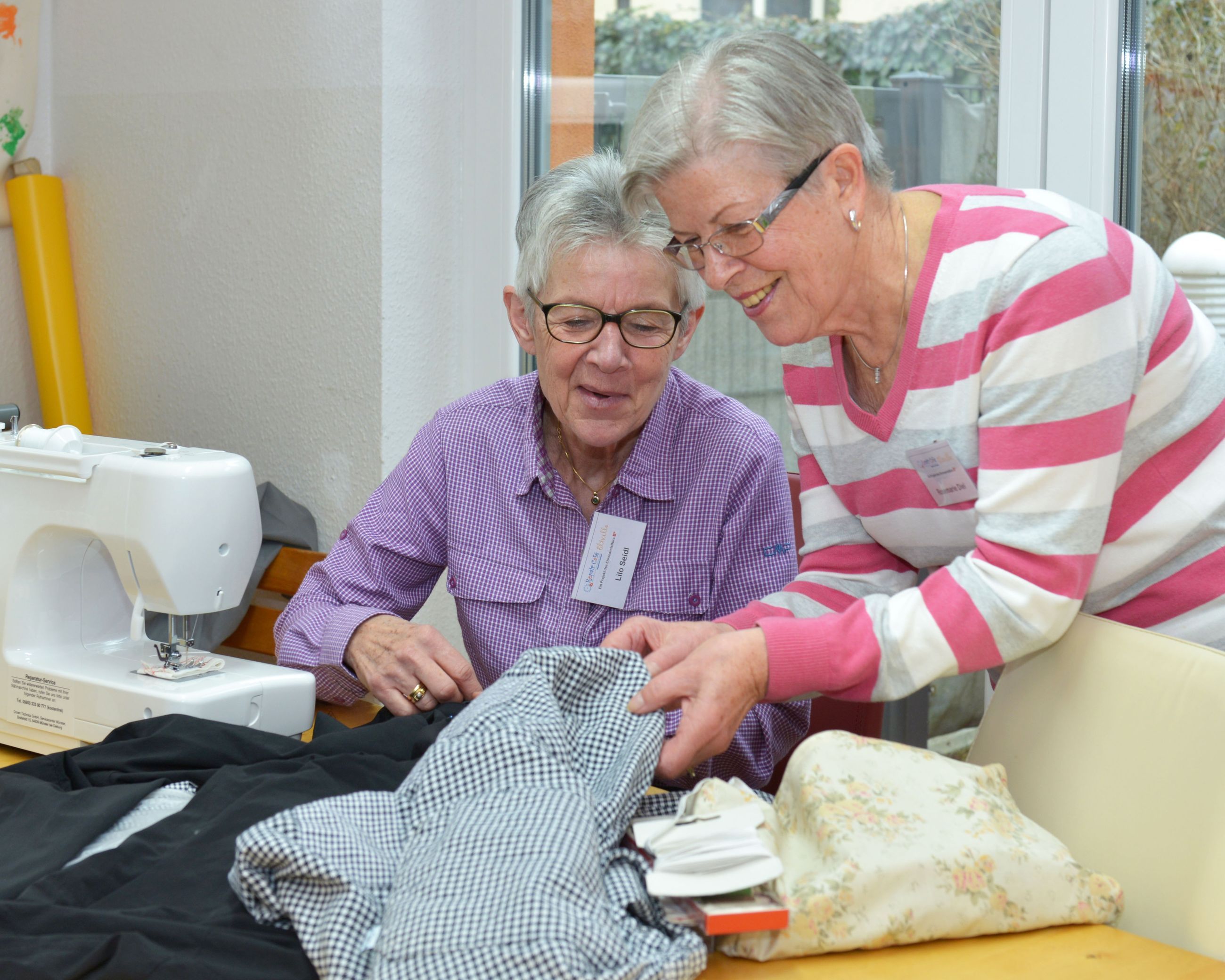 Zwei Damen reparieren defekte Kleidung an einer Nähmaschine.
