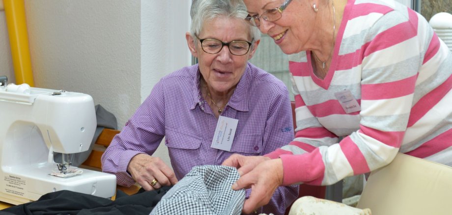 Zwei Damen reparieren defekte Kleidung an einer Nähmaschine.
