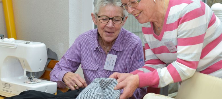 Zwei Damen reparieren defekte Kleidung an einer Nähmaschine.