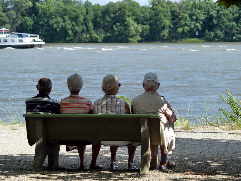 Vier Senioren sitzen auf einer Bank am Rheinufer.
