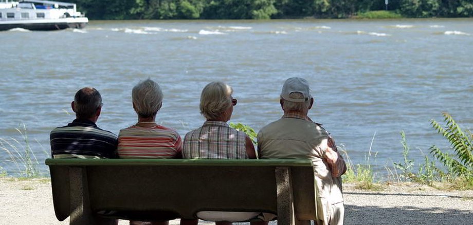 Vier Senioren sitzen auf einer Bank am Rheinufer.