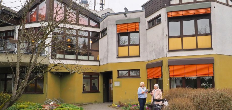 Die Gemeindepflegerin sitzt im Seniorenbüro in Eltville. Ein Seniorenheim vom außen - davor stehen die Gemeindepflegerin und eine Seniorin.