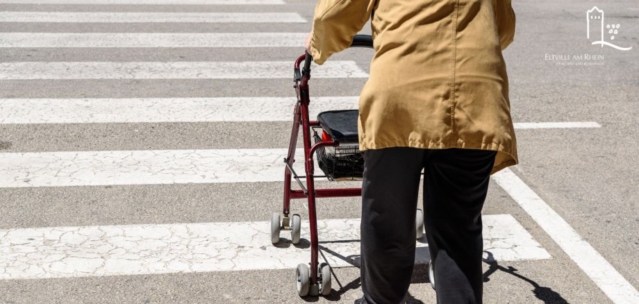 Symbolbild Person von hinten geht mit einem Rollator über einen Zebrastreifen