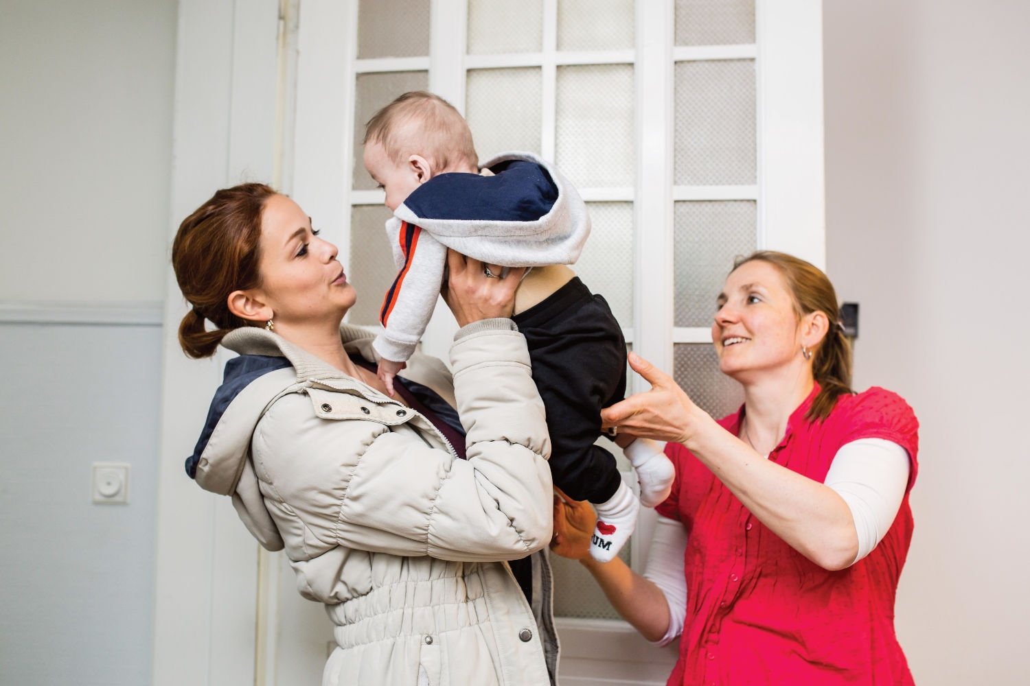 Eine Mutter hebt ihr Kind hoch, nebendran steht eine wellcome-Unterstützerin. 