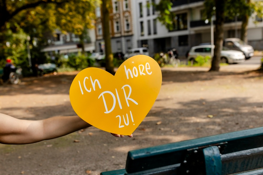 Symbolbild gelbes Herz mit Aufschrift "Ich höre dir zu" und einer Bank im Hintergrund