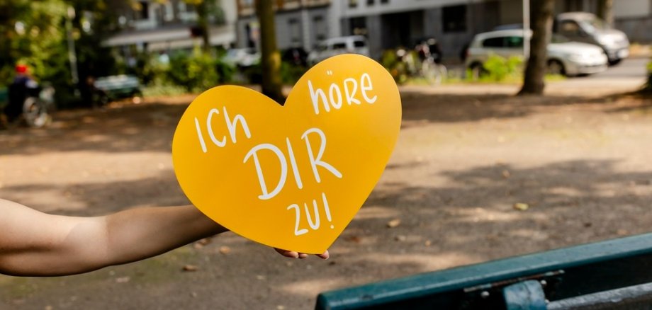 Symbolbild gelbes Herz mit Aufschrift "Ich höre dir zu" und einer Bank im Hintergrund