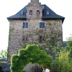 Die Hattenheimer Burg: Burg mit hohem Schornstein und Torbogen am Eingang, der mit Efeu bewachsen ist.