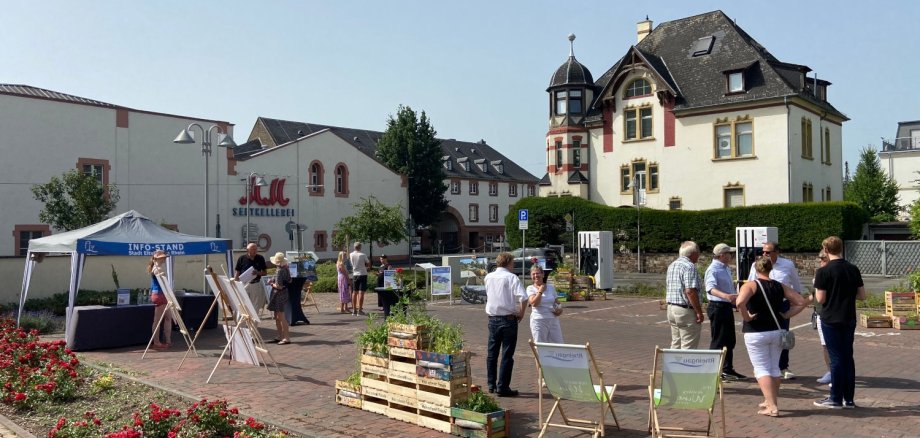 Mehrere Besucher stehen in Gruppen auf dem Parkplatz am Kiliansring, der mit einem Infostand der Stadt, Pflanzkisten und den Animationen zur Neugestaltung geschmückt ist.