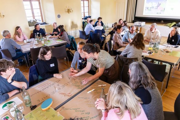 Alle Beteiligten an Projekttischen am Diskutieren