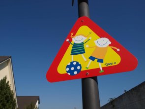 In Eltville am Rhein gibt es zahlreiche Spiel- und Bolzplätze und sogar zwei Fitnessparcours und einen Skaterpark. Buntes Straßenschild mit zwei Ballspielenden Kindern.