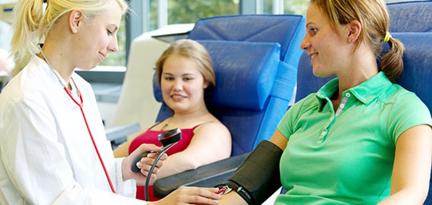 Zwei Frauen auf Liegen vor der Blutspende, eine Ärztin misst bei einer der beiden den Blutdruck