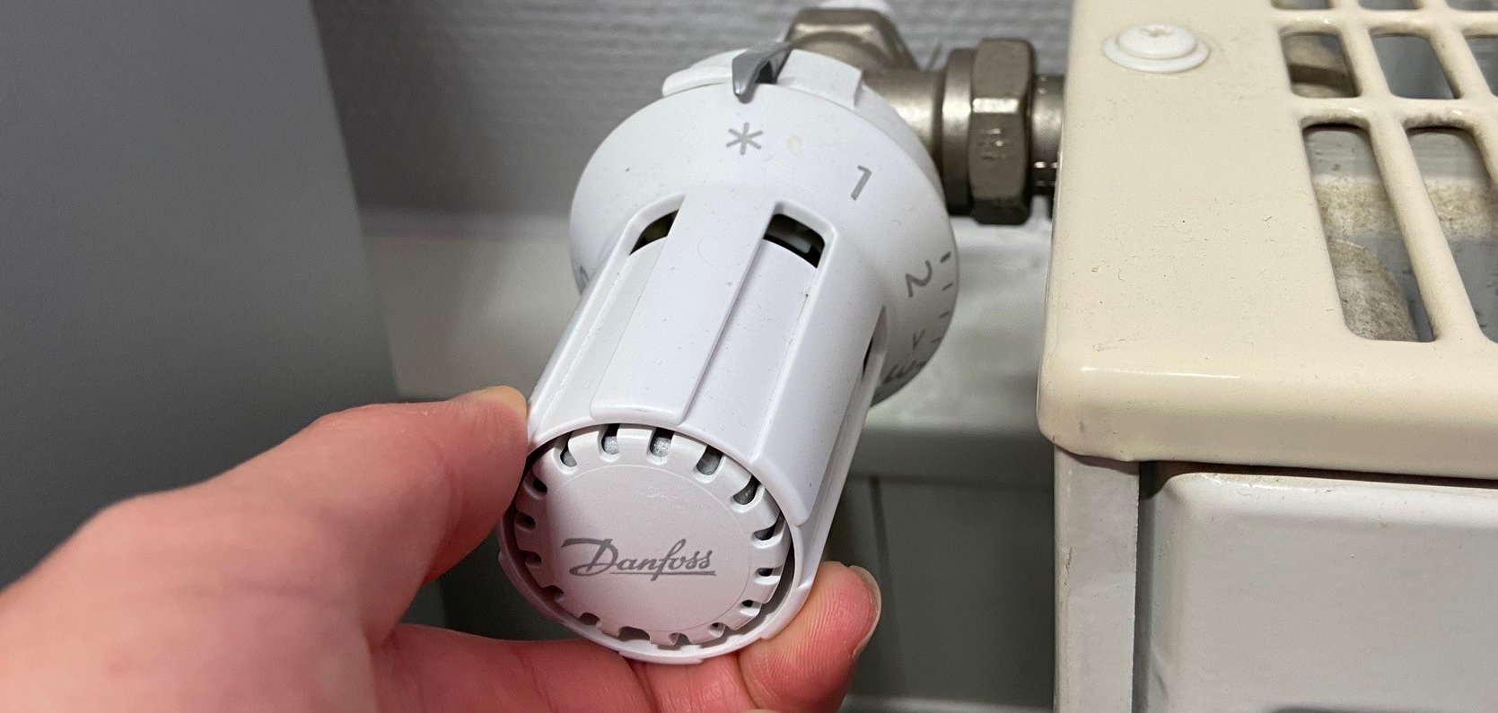 Hand dreht an einem Heizkörper-Knauf.