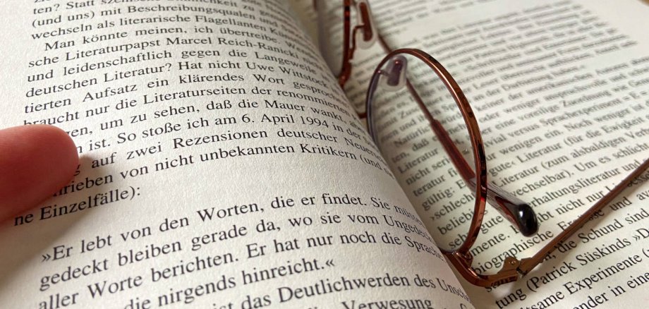 Auf einem aufgeklappten Buch liegt eine Brille.