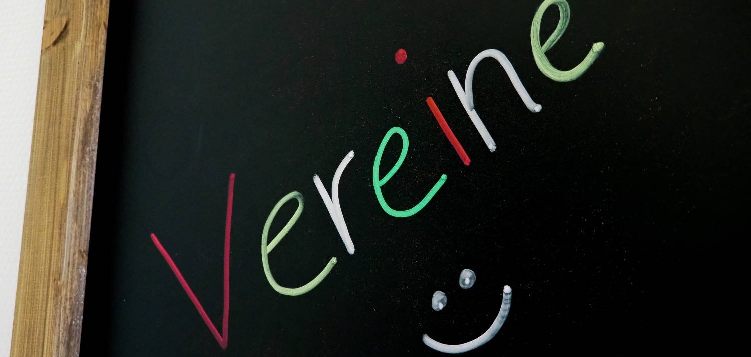 Auf einer schwarzen Tafel steht mit bunter Kreide "Vereine" geschrieben.