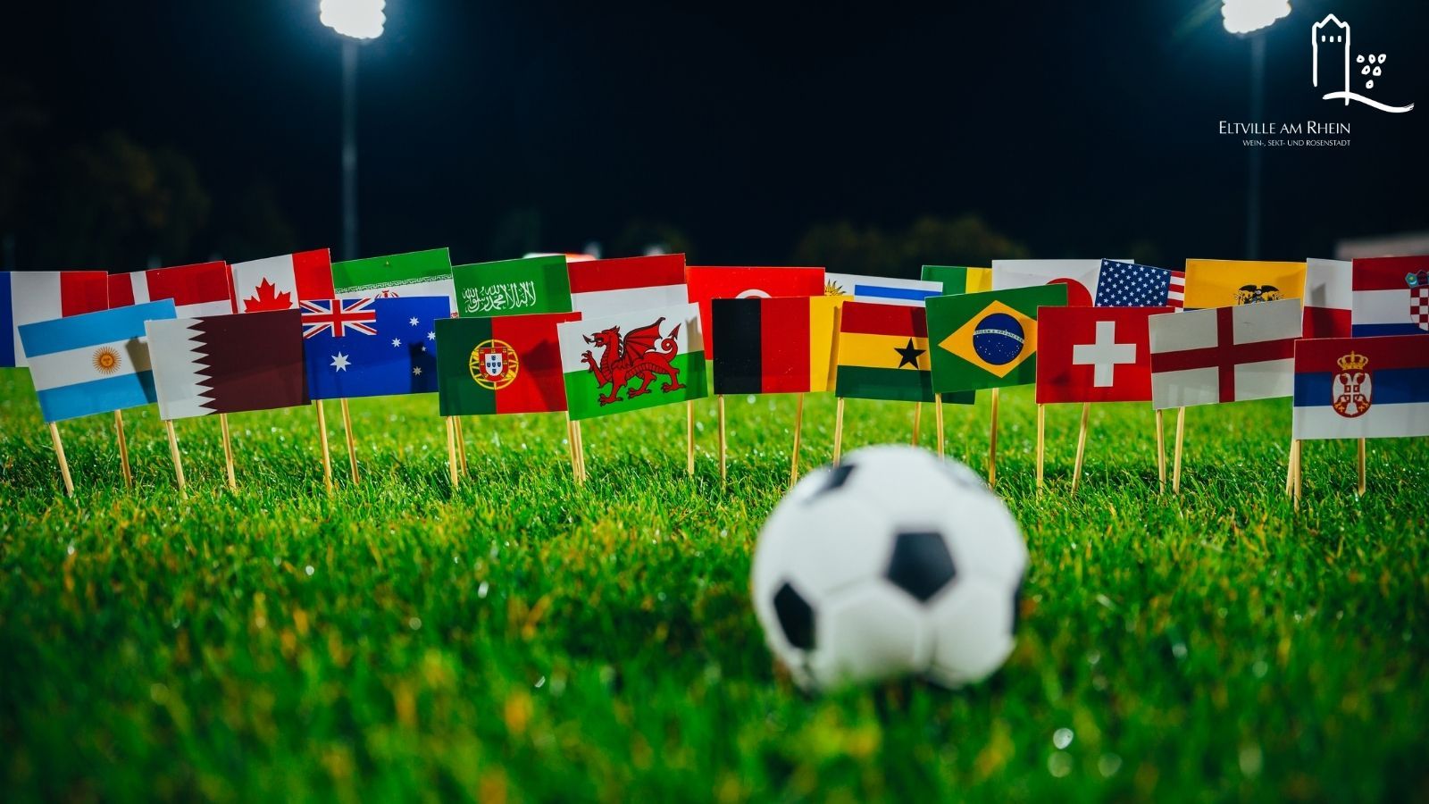 Symbolbild Fußball auf Rasen mit Flaggen verschiedenster Länder im Hintergrund