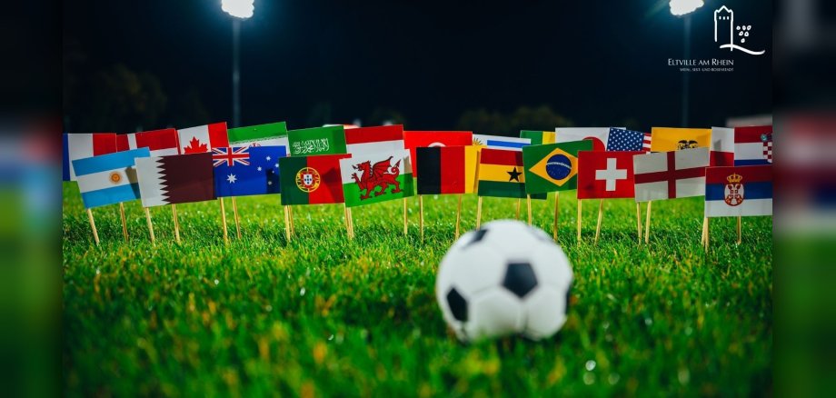 Symbolbild Fußball auf Rasen mit Flaggen verschiedenster Länder im Hintergrund