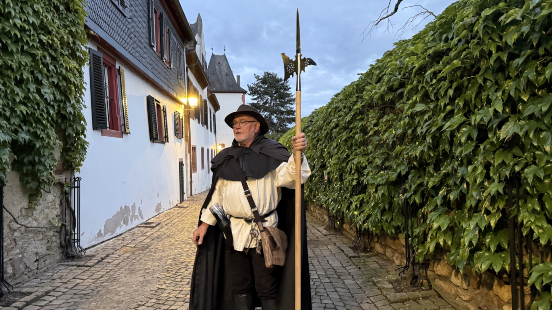 Ein Mann in historischer Kleidung mit einer Hellebarde in einer Altstadtgasse