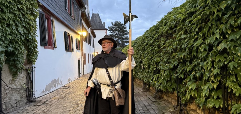 Ein Mann in historischer Kleidung mit einer Hellebarde in einer Altstadtgasse