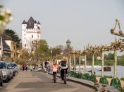 Eine Frau und ein Kind auf Fahrrädern fahren am Rheinufer in Richtung Burgturm.