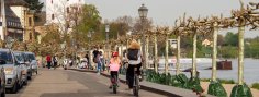 Eine Frau und ein Kind auf Fahrrädern fahren am Rheinufer in Richtung Burgturm.