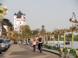 Eine Frau und ein Kind auf Fahrrädern fahren am Rheinufer in Richtung Burgturm.