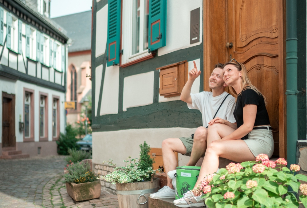 Ein Mann und eine Frau sitzen mit der Walk like a local-Tasche auf Treppenstufen in der Altstadt in Eltville