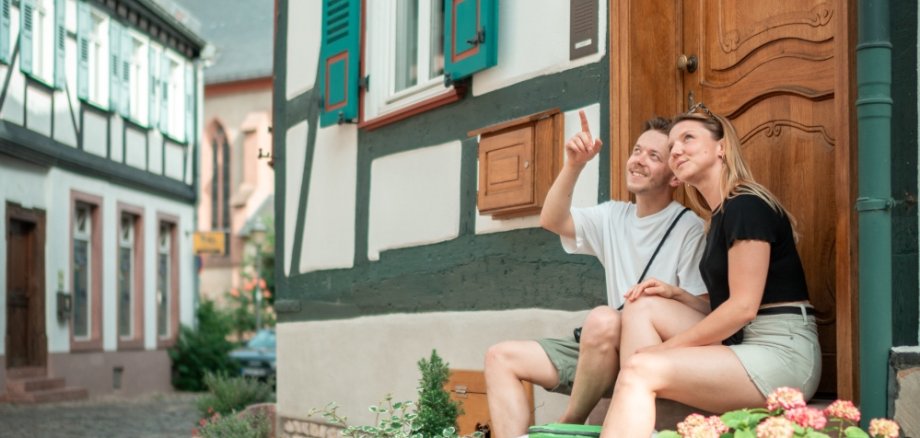 Ein Mann und eine Frau sitzen mit der Walk like a local-Tasche auf Treppenstufen in der Altstadt in Eltville