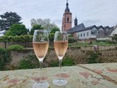 Zwei Sektgläser gefüllt mit Rosé-Sekt stehen auf einer Mauer, Kirchturm im Hintergrund zu sehen