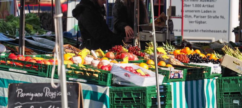 An einem Stand verkauft eine Frau frisches Obst und Gemüse.