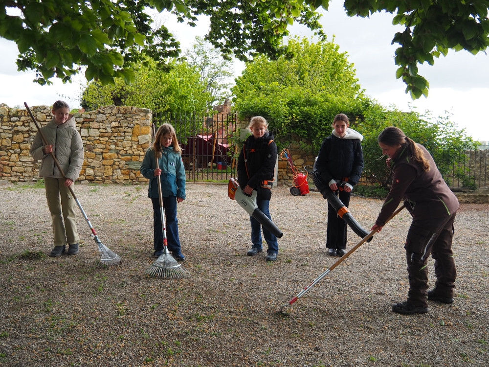 Schülerinnen und Gärtnerin beim Harken und Laub blasen