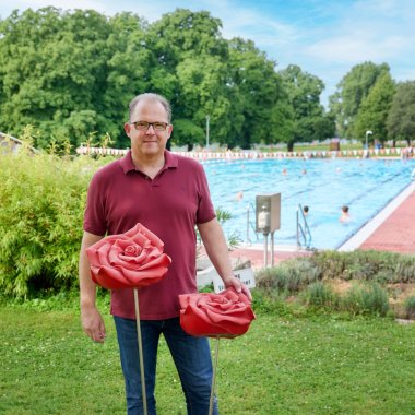 Bürgermeister Kunkel steht an roten Metallrosen im Freibad