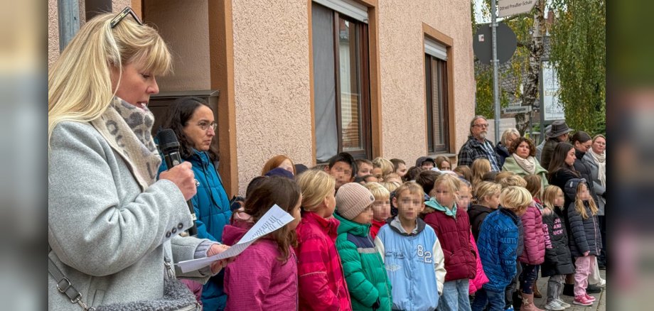Am linken Rand steht Sabine Gebauer und trägt etwas vor, die Grundschulkinder stehen nebeneinander und hören zu