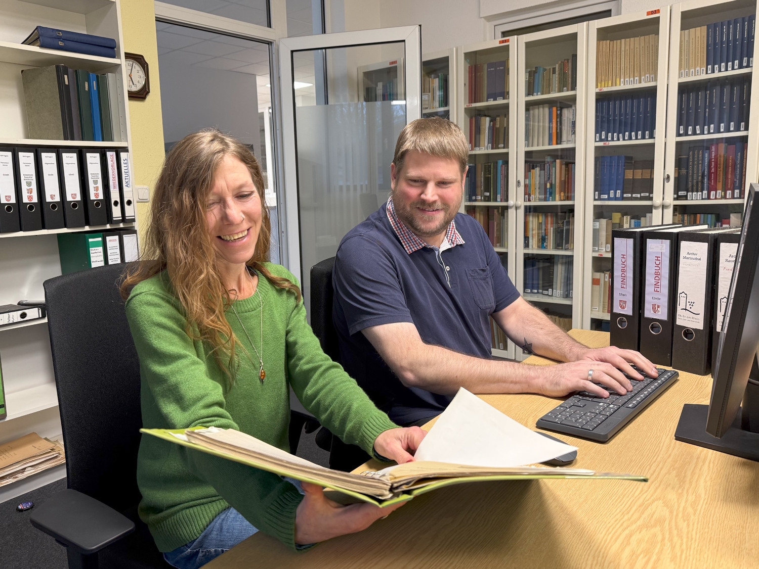 Mirjam Ehlers mit einem Findbuch in der Hand und Björn David beim Tippen auf der Tastatur