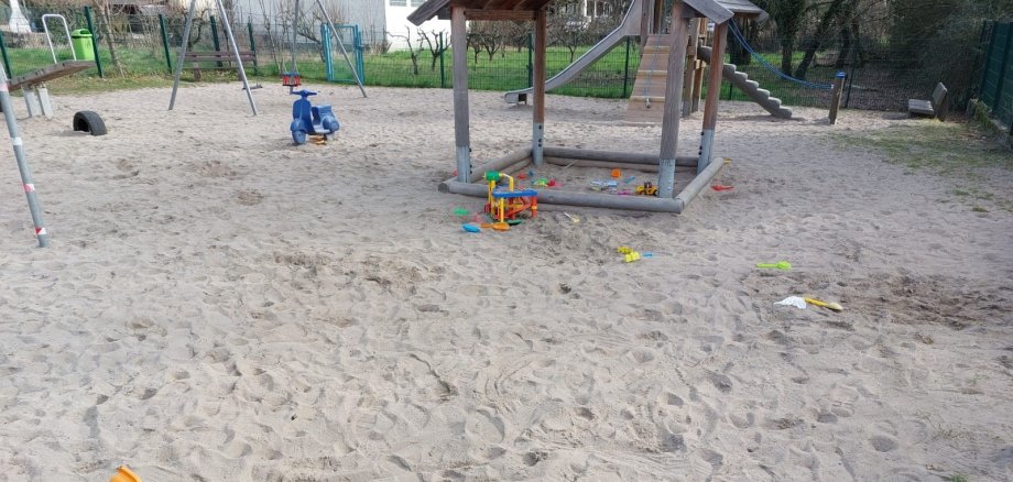Sandkasten auf einem Spielplatz mit einigen bunten Plastikspielsachen