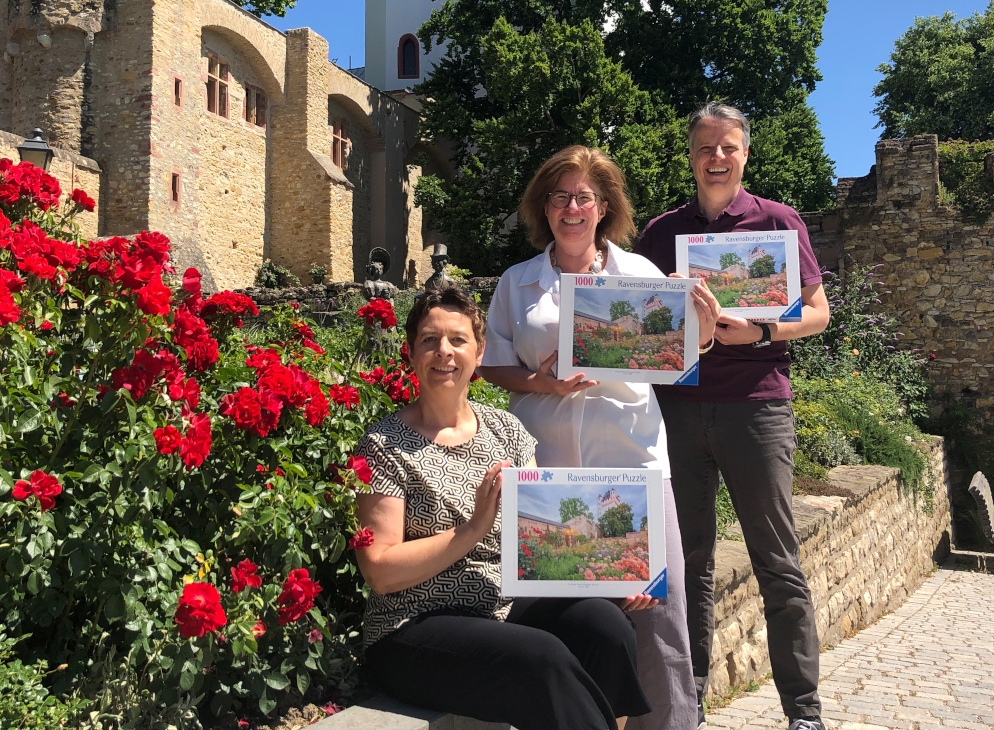 Dier drei Beteiligten mit Puzzle-Kartons vor dem Motiv