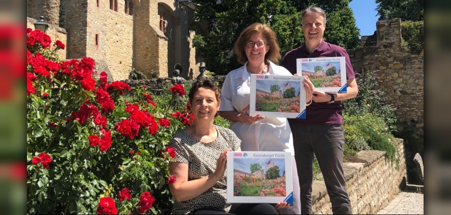 Dier drei Beteiligten mit Puzzle-Kartons vor dem Motiv