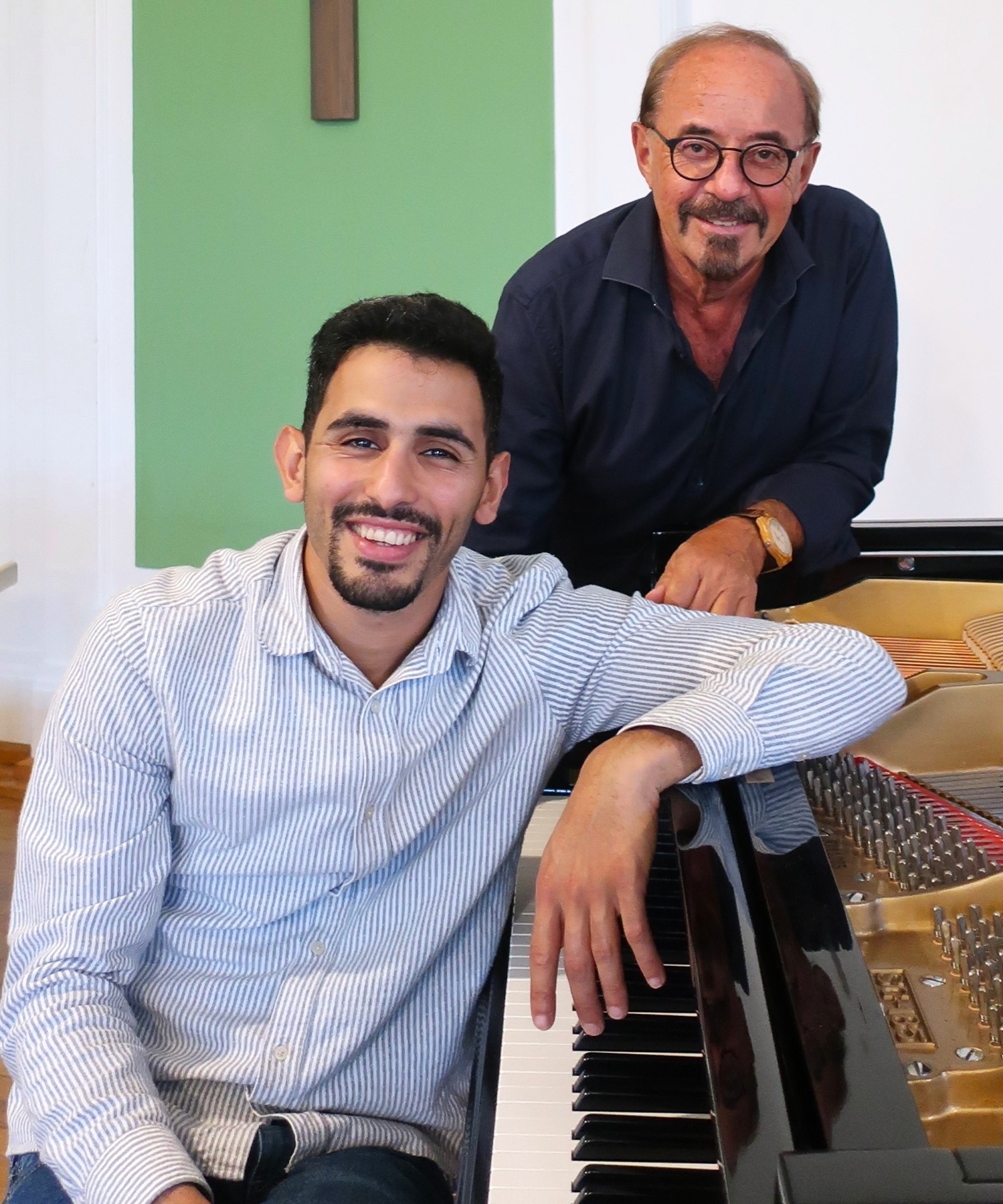 Aeham Ahmad sitzt am Klavier, Andreas Lukas steht hinter ihm, ebenfalls ans Klavier lehnend