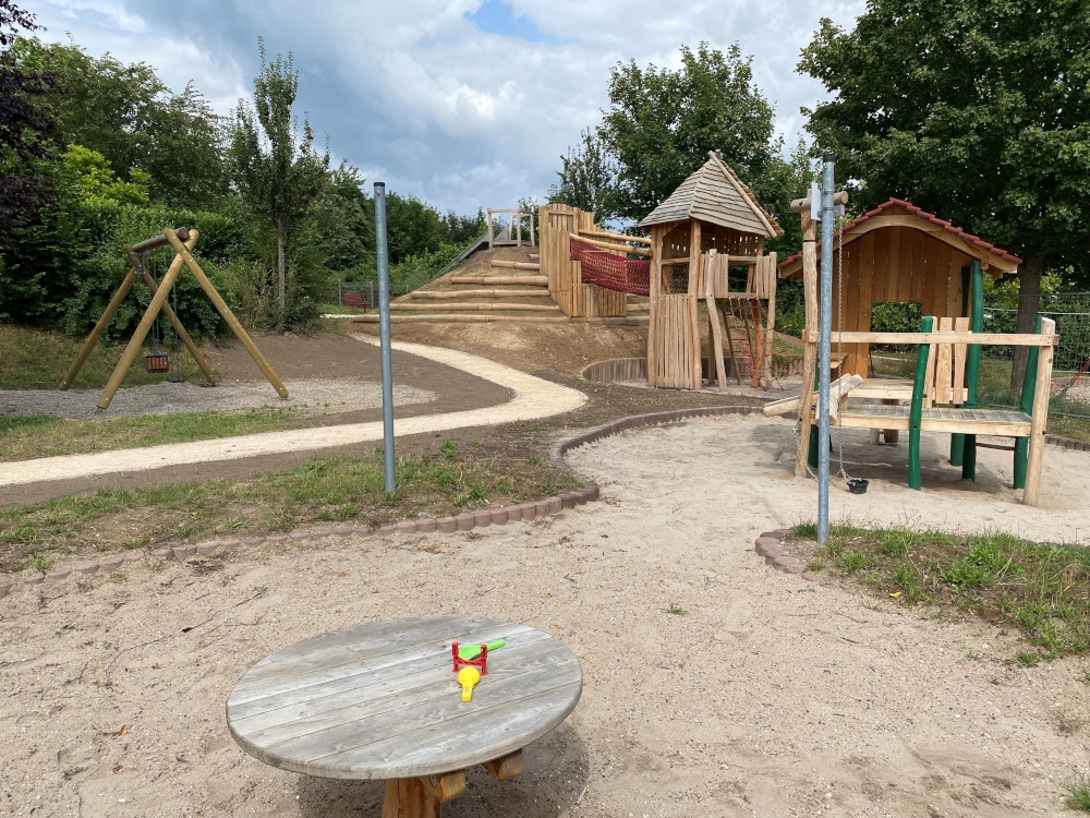 Blick auf dem Spielplatz mit Sandkasten, Kletterturm und Rutschenhügel mit Rutsche