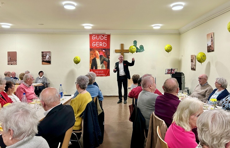 "Gude Gert" auf der Bühne, die Zuschauerinnen udn Zuschauer sitzend an Tischen