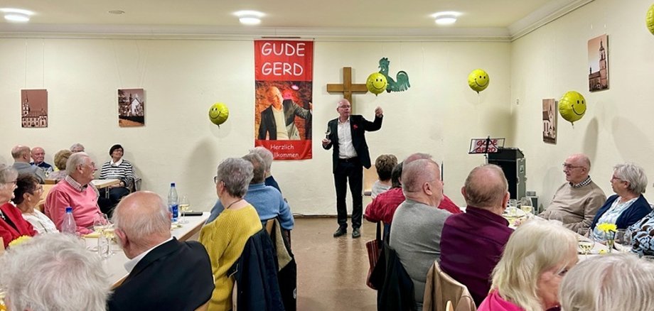 "Gude Gert" auf der Bühne, die Zuschauerinnen udn Zuschauer sitzend an Tischen