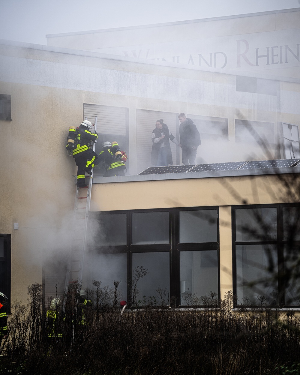 Feuerwehrleute steigen durch ein Fenster ein, durch das Rauch kommt