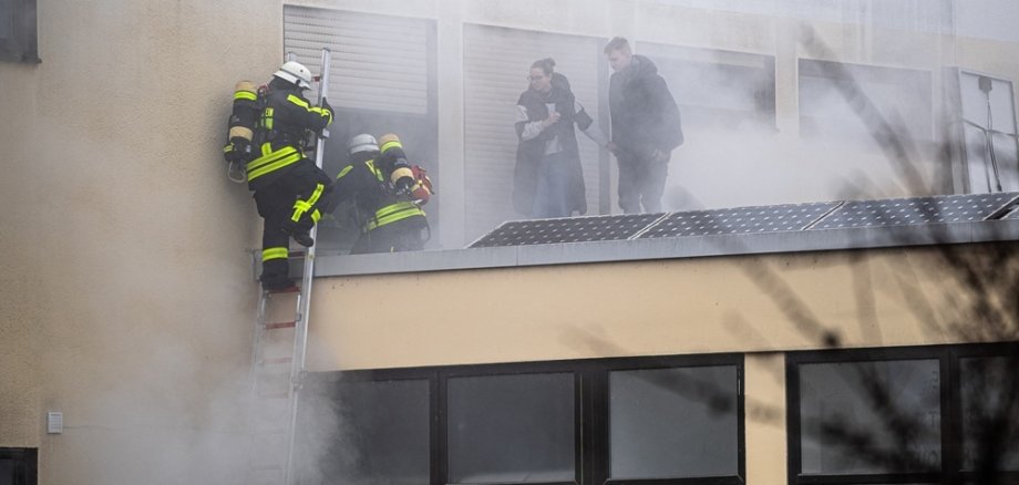 Feuerwehrleute steigen durch ein Fenster ein, durch das Rauch kommt
