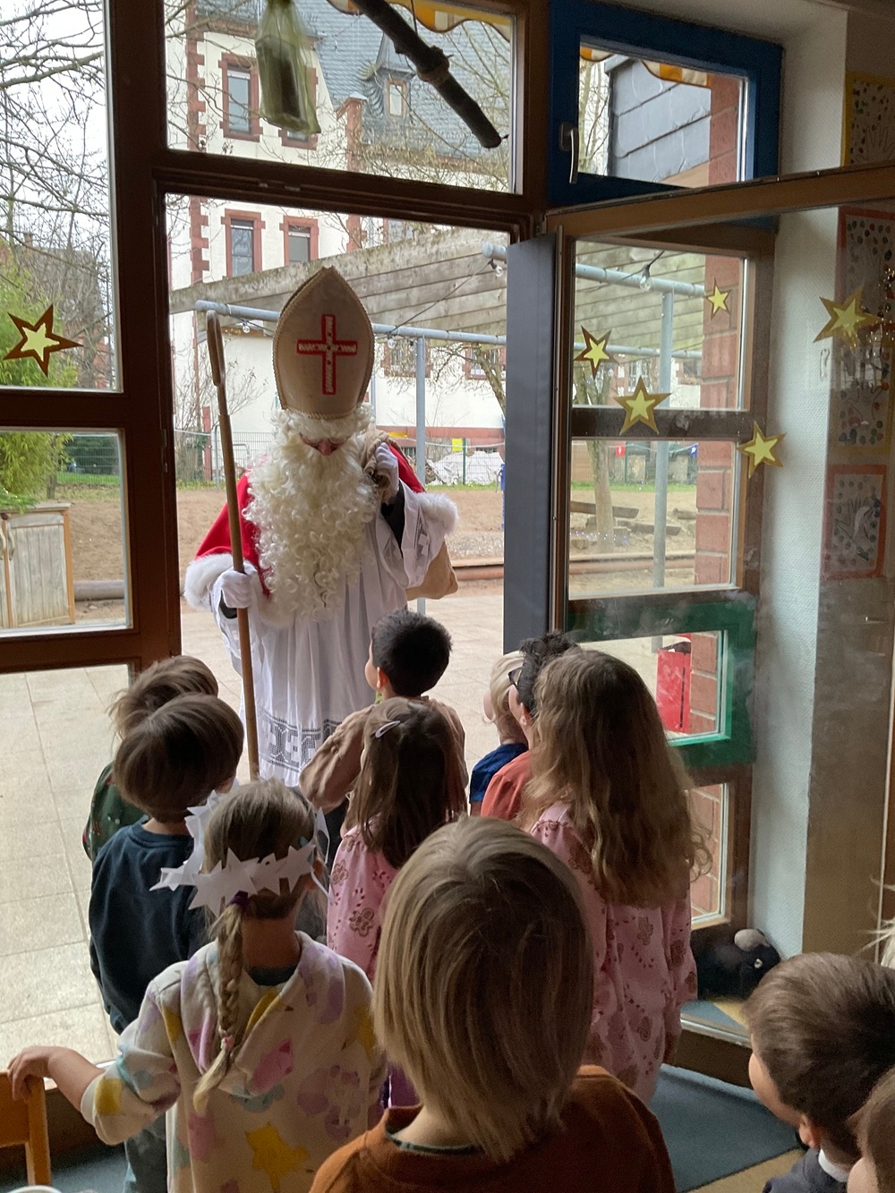 Als Nikolaus verkleideter Mann kommt in die Kita, Kitakinder sind von hinten zu sehen, wie sie ihm empfangen an der Tür